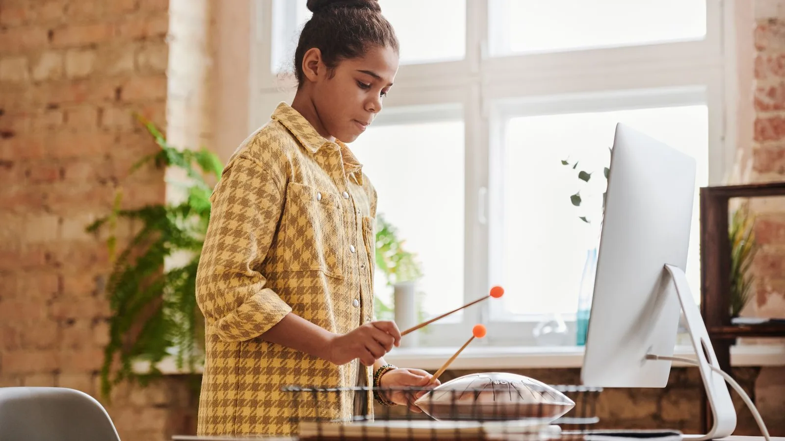 Jeune musicienne jouant du handpan avec deux maillets devant un écran